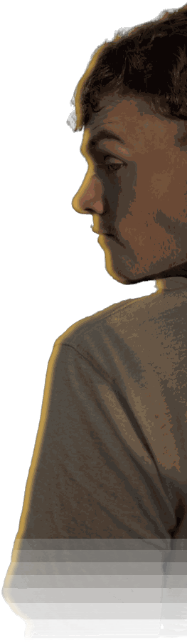 Cathal Kelley in profile, looking off to the side, lit in dramatic gold