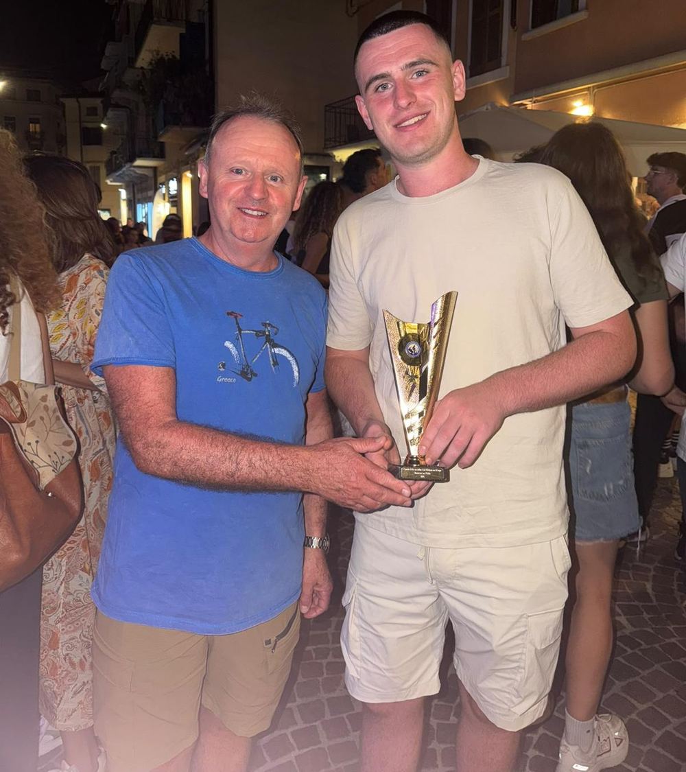 A father and son holding a small gold trophy together on a busy street at night
